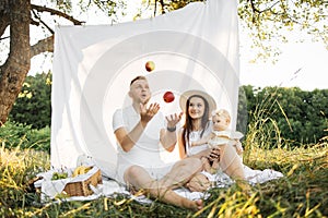 Happy young family having picnic sitting on white blanket outdoors.