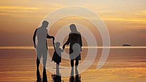 Happy young family holding hands each other walking along the shore during amazing golden sunset. Family holiday. slow