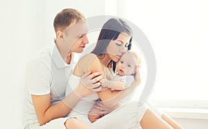 Happy young family at home in white room near window, parents baby together