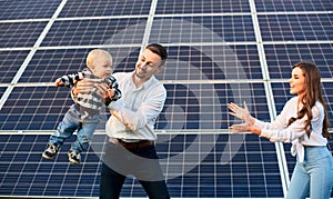Happy young family with a little blond child having fun on the background of solar panels