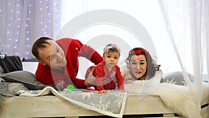 Happy young family is lying on the bed, smiling and looking at the camera