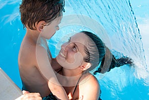 Happy young family of mother woman and little wet child in swimming pool under waterfall jet turquoise spa hydrotherapy water