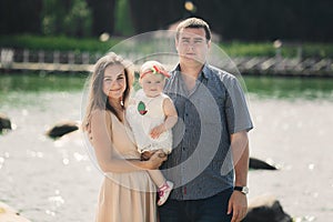 Happy young family near lake, pond. Family enjoying life together at meadow. People having fun in nature. Family bonds