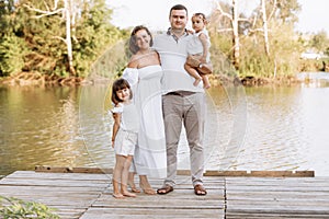 Happy young family near lake, pond on summer on countryside. Mother, father and two child daughter smiling and having