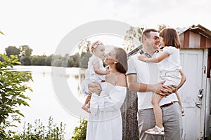 Happy young family near lake, pond on summer on countryside. Mother, father and two child daughter smiling and having