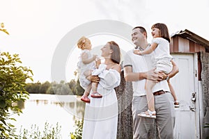 Happy young family near lake, pond on summer on countryside. Mother, father and two child daughter smiling and having