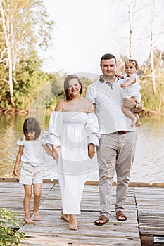 Happy young family near lake, pond on summer on countryside. Mother, father and two child daughter smiling and having