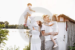 Happy young family near lake, pond on summer on countryside. Mother, father and two child daughter smiling and having