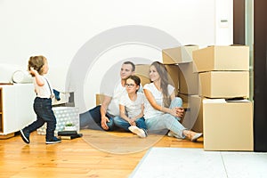 Happy young family, parents daughter and son, unpacking boxes and moving into a new home. funny kids run in with boxes