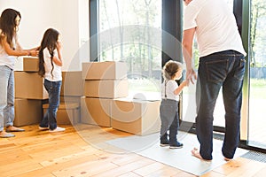 Happy young family, parents daughter and son, unpacking boxes and moving into a new home. funny kids run in with boxes