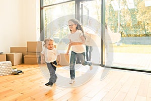 Happy young family, parents daughter and son, unpacking boxes and moving into a new home. funny kids run in with boxes