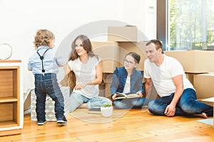 Happy young family, parents daughter and son, unpacking boxes and moving into a new home. funny kids run in with boxes