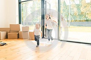 Happy young family, parents daughter and son, unpacking boxes and moving into a new home. funny kids run in with boxes