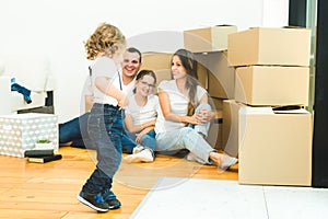 Happy young family, parents daughter and son, unpacking boxes and moving into a new home. funny kids run in with boxes