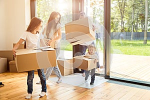 Happy young family, parents daughter and son, unpacking boxes and moving into a new home. funny kids run in with boxes