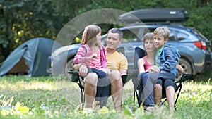 Happy young family parents and kids sitting together at campsite in summer talking happily together.