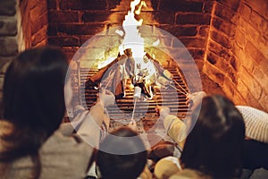 Happy young family parents with two small kids gathering around brick fireplace in cozy and warm country house during Christmas