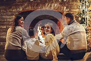 Happy young family parents with two small kids gathering around fireplace during Christmas holidays