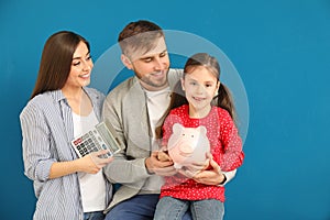 Happy young family with piggy bank and calculator on color background