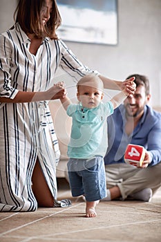 Happy young family playing and baby learning to walk at home