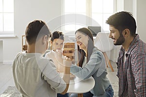 Happy young family plays with their children and take turns removing bricks from a wooden tower.