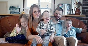 Happy young family portrait, Caucasian parents and three cute kids looking at camera at home on the couch slow motion.