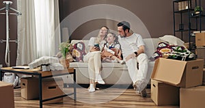 Happy young family preschooler daughter husband and wife sitting on cozy comfortable sofa in new apartment relxing after