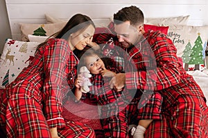 Happy young family in red pajamas lie on the bed on Christmas Eve in their apartment with New Year`s decor