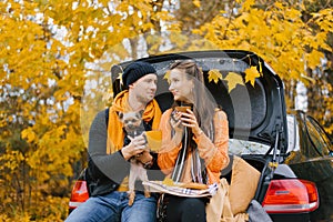 A happy young family is relaxing after a day spent outdoors in the autumn forest. A couple in love is sitting in the trunk of a
