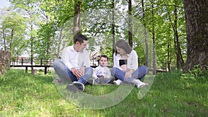 A happy young family is resting in the park. A wife with her husband and child relaxing in nature