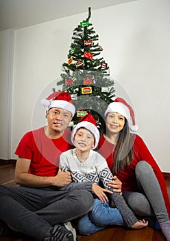 Happy young family sitting by Christmas tree