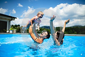 Young family with small daughter in swimming pool outdoors in backyard garden, playing. photo