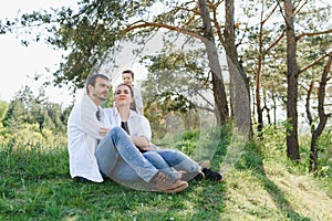 Happy young family spending time outdoor on a summer day have fun at beautiful park in nature while sitting on the green grass.