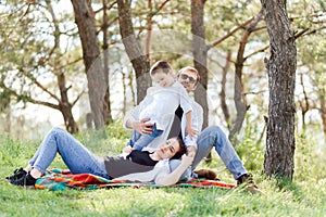 Happy young family spending time outdoor on a summer day have fun at beautiful park in nature while sitting on the green grass.