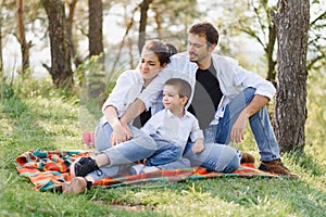 Happy young family spending time outdoor on a summer day have fun at beautiful park in nature while sitting on the green grass.