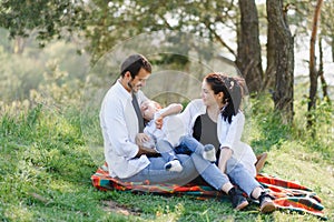 Happy young family spending time outdoor on a summer day have fun at beautiful park in nature while sitting on the green grass.