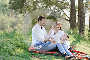 Happy young family spending time outdoor on a summer day have fun at beautiful park in nature while sitting on the green grass.