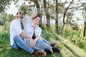 Happy young family spending time outdoor on a summer day have fun at beautiful park in nature while sitting on the green grass.