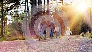 Happy young family taking a walk in a park, back view. Family holding hands walking together along forrest path with their daughte