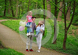 Happy young family with their two children are walking in summer forest park, parenthood vacations with kids