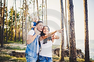 Happy young family of three people resting in a park outside the city. daughter sits at daddy on shoulders, and parents show direc