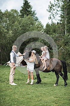 Happy young family with two children, wearing stylish casual boho clothes and beautiful horse in the forest or meadow
