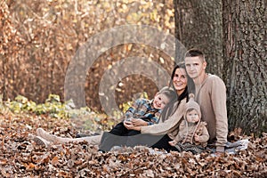 Happy young family with two little children relaxing and having fun in autumn park on sunny day