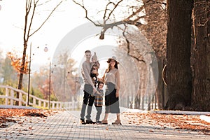 Happy young family with two little children walking and having fun in autumn park on sunny day