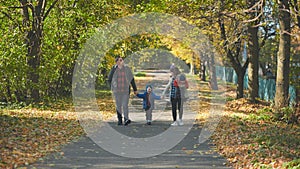 A happy young family walks along a city park road in the fall.