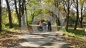 A happy young family walks along a city park road in the fall.