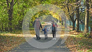 A happy young family walks along a city park road in the fall.