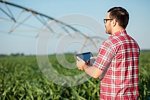 Happy young farmer or agronomist controlling large irrigation system with a tablet