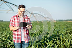 Happy young farmer or agronomist using a tablet in corn field. Irrigation system in the background