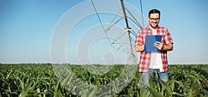 Happy young farmer or agronomist writing on a clipboard, inspecting a corn field. Wide ratio panoramic photo